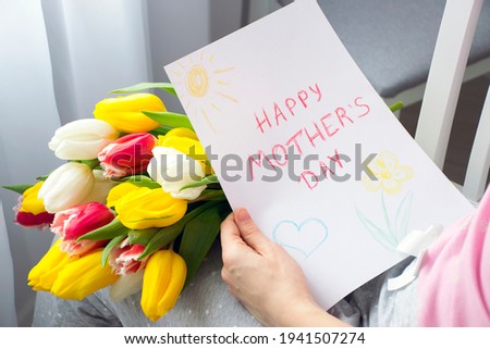 Child's drawing Happy Mother`s Day greeting card  and bouquet of flowers colorful tulips in mother`s hands. Srprise for Mom on Mother`s Day celebration.