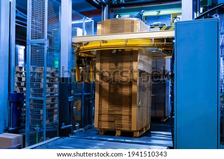 Industrial equipment - typical stretch wrapping machine in process of work. Packaging of corrugated cardboard. Selective focus. Royalty-Free Stock Photo #1941510343