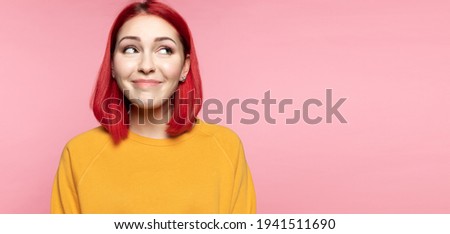 Modern young pink haired shy girl looking aside, feeling embarrassed. Smiling bashful confused caucasian female dreaming imagining idea on pink studio background. Human emotions, modest person concept Royalty-Free Stock Photo #1941511690