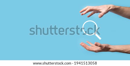 Male hand holding magnifying glass ,search icon on blue background. Concept search engine optimization, customer support.Browsing Internet Data Information.Networking Concept