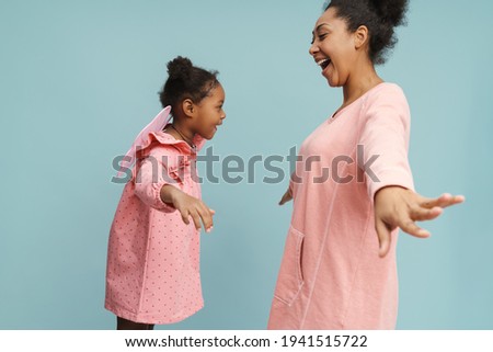 Happy black mother and daughter with butterfly wings making fun together isolated over blue background
