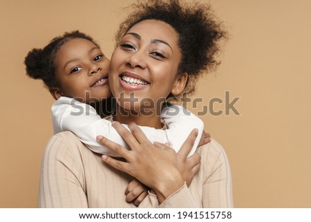 Happy black mother and daughter hugging and smiling isolated over beige background