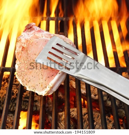 Bone steak held tongs over a hot grill and flames in the background, you can also see more pictures of BBQ in my set