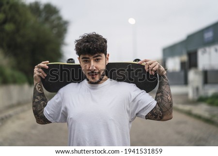 A young confident European male holding a skate on blurred background of a street