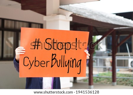 Text Stop cyber bullying on paper sign held by Asian girl student. Concept for calling everybody to stop bullying by using bad word and bad texting  social  media online or messaging platforms.