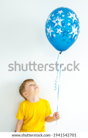 A beautifull male child in a yellow T-shirt and shorts holds a blue ball in his hands on a white background .caucasian.
concept - children, holiday, birthday
Selective focus.

