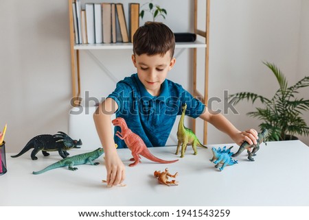 Focused kid playing with dinosaurs at home. Boy learning paleontology by dino toys at leisure. Concept of clever child and early education Royalty-Free Stock Photo #1941543259