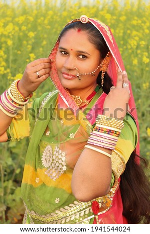 beautiful Rajput (Rajasthani) woman puts veil in her dress of culture and she is standing in mustard field. close-up.