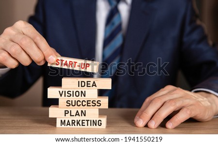 Man in suit building wooden blocks with text START-UP, ideas, vision, success, plan, marketing. Investor accelerate start-up project concept.