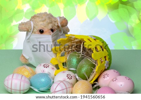Happy Easter greeting card. Closeup of colorful easter eggs, a basket and a lamb with mask on green table against abstract blurred spring background. Religion and culture concept.