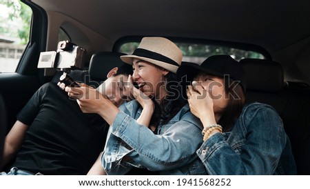 Friend group making selfie vlog video together in car during traveling trip.