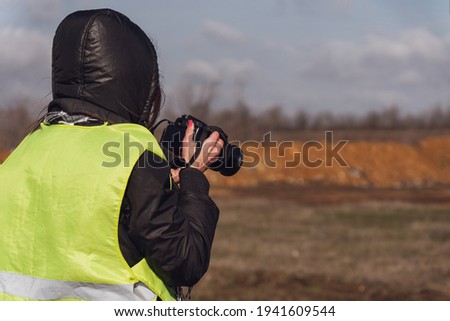 Girl photographer in a yellow rescue vest with a camera in her hands. Back view, no face, copy space