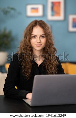 Head shot young student sitting at table with computer, working remotely, writing email or reading news. Young woman attending distant educational courses, planning job or communicating online.