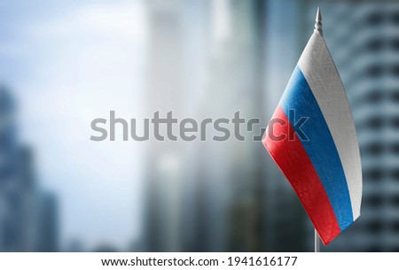 A small flag of Russia on the background of an urban abstract blurred background. Royalty-Free Stock Photo #1941616177