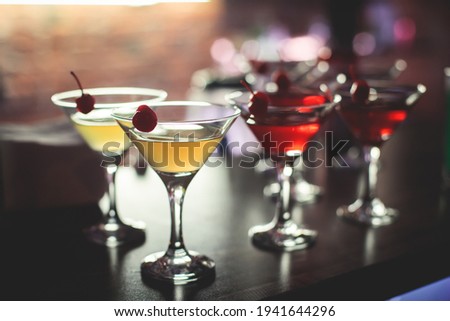 View of different coloured alcohol beverage cocktail drinks setting on bar counter in the night club party, tequila,  glasses with martini, vodka, spritz and others on decorated catering banquet table