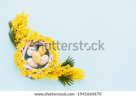 Easter wreath with eggs and mimosa flowers on blue background. Top view, copy space for text
