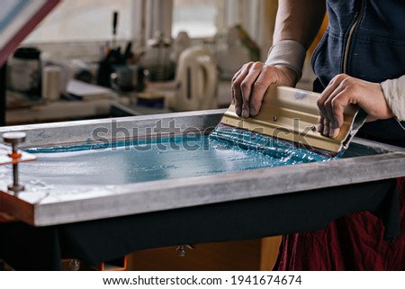 selective focus photo of male hands with squeegee. serigraphy production. printing images on t-shirts by silkscreen method in a design studio Royalty-Free Stock Photo #1941674674
