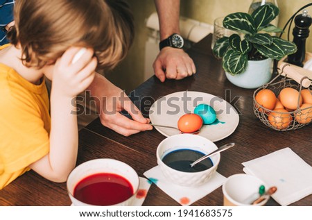 Easter day. Father and son painting eggs on wooden background. Family sitting in a kitchen. Preparing for Easter, creative homemade decoration.