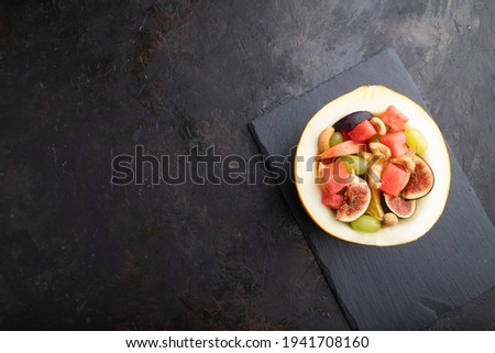 Vegetarian fruit salad of watermelon, grapes, figs, pear, orange, cashew  on slate board on a black concrete background. Top view, flat lay, copy space.