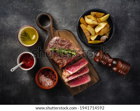 Sliced grilled meat steak New York Striploin with sauce and potato on wooden board on grey background. Top view. Royalty-Free Stock Photo #1941714592