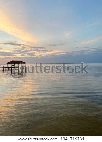 Colorful sunset over bay water with pier and hammock hanging