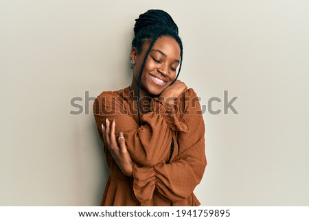 African american woman with braided hair wearing casual brown shirt hugging oneself happy and positive, smiling confident. self love and self care  Royalty-Free Stock Photo #1941759895