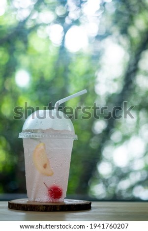 Glass of cold pink fresh lychee juice soda on wood plate with nature background