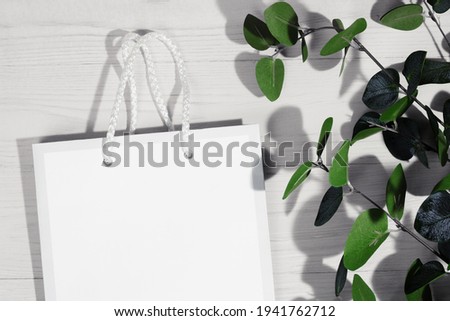 Product advertising background. White paper pocket bag on a wooden background with leaves and shadows. Top view. Copy space.