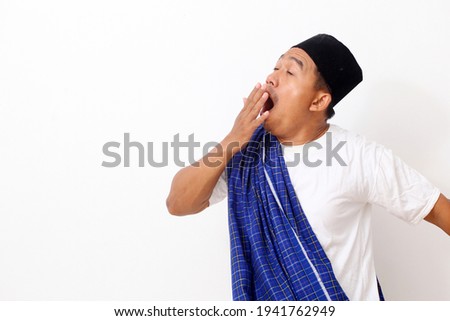 Portrait of funny Asian man yawning and showing a sleepy gesture. Isolated on white background