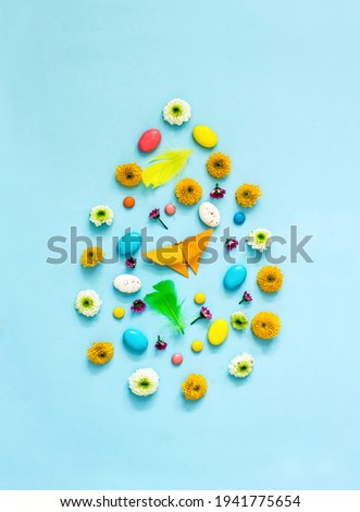 Creative Easter egg made of flowers,
 colored eggs, feathers, origami rabbits and butterflies, sweets on a blue background. Creative easter composition, flat lay