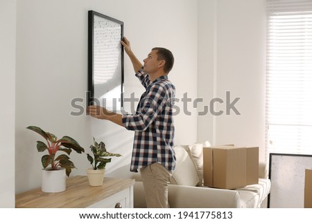 Man hanging picture on white wall in room. Interior design