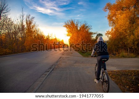 cyclist riding a bike lane next to a highway in an autumn forest at sunset