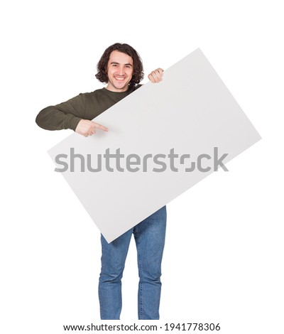 Contented young man holding a big blank banner for advertising pointing and showing with index finger. Happy guy with an empty sheet for text announcements as a lottery winner with bank check prize Royalty-Free Stock Photo #1941778306