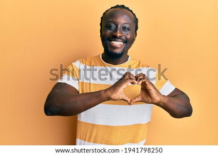 Handsome young black man wearing casual yellow tshirt smiling in love showing heart symbol and shape with hands. romantic concept. 