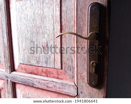 the door handle made of old brass on the old wooden door is faded red