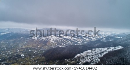 A beautiful landscape shot from a drone. A small village located near mountains and a forest covered with snow in foggy cloudy weather. Recreation, tourism concept.