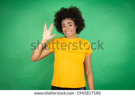 African american woman wearing orange casual shirt over green background doing hand symbol