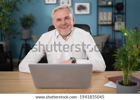 Serious senior man sit at cozy home office table working on laptop, 55s businessman consider about issue, solve business remotely texting e-mail. Older generation advanced user of modern tech concept