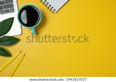 Desk top view on yellow background. Flat lay, top view office table desk. Workspace with Laptop, keyboard, coffee, pencil, green leaf and blank note.