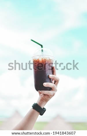 Closeup of hand holds a glass cup of mocha coffee to beautiful , calm blue sky and front in sunny morning.