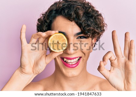 Young man wearing woman make up holding lemon doing ok sign with fingers, smiling friendly gesturing excellent symbol 