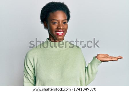 Young african american girl wearing casual clothes smiling cheerful presenting and pointing with palm of hand looking at the camera. 