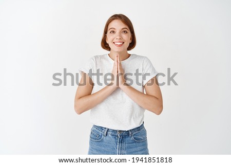 Pretty please. Cute young woman holding hands in begging sign, asking for help, need favour, smiling cute, standing on white background