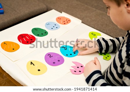 Different color paper eggs on white table. Easter theme game, find other side of figure.