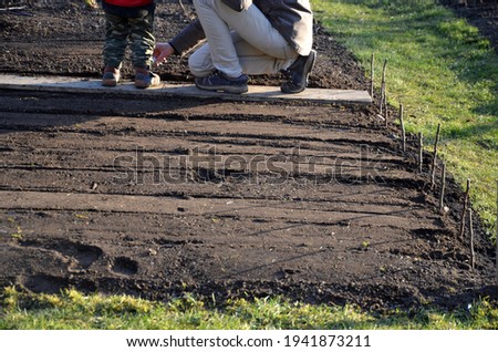 spring sowing of vegetables in the home environment of a green garden with a grass path. mother with little boy gardening at coronavirus time are closed nursery. they walk on the board 