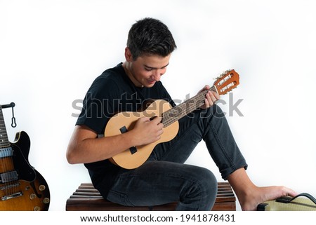 Teenager playing guitar sitting on a trunk, with a white background. Musician concept.