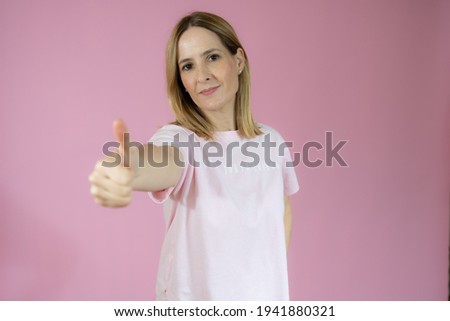 Smiling pretty young woman showing thumb up isolated over pink background