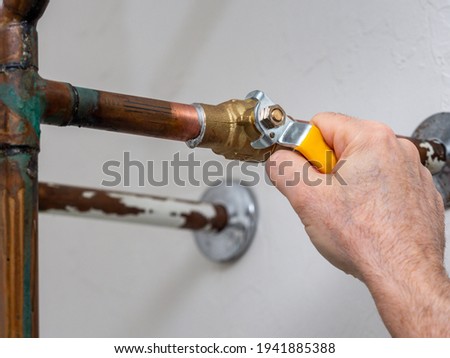 Plumber turning water shut off valve. Copper plumbing pipe with brass water supply valve and yellow stopcock handle. Royalty-Free Stock Photo #1941885388