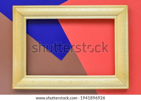 Empty wooden frame on multi-colored abstract paper background. Top view. Copy space. Selective focus. 