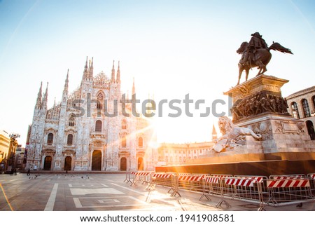 Milan, Italy - March 2021: Wide angle view of Milan Cathedral (Duomo di Milano) with sun illuminating the empty square, cordoned off statue, postcard